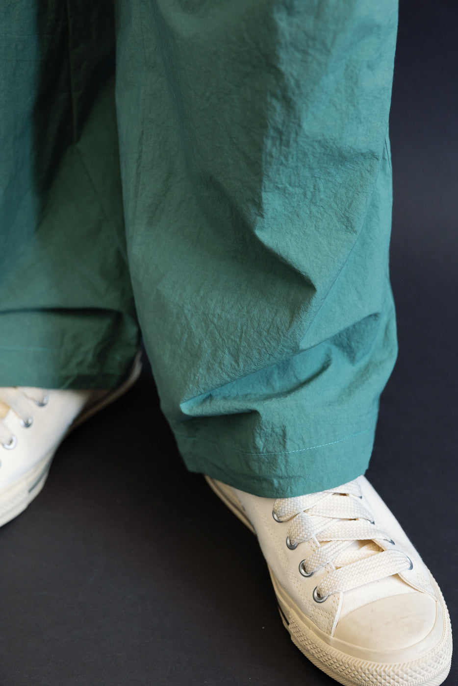 Close-up front view of teal wide-leg pants hem with white sneakers, worn by male model
