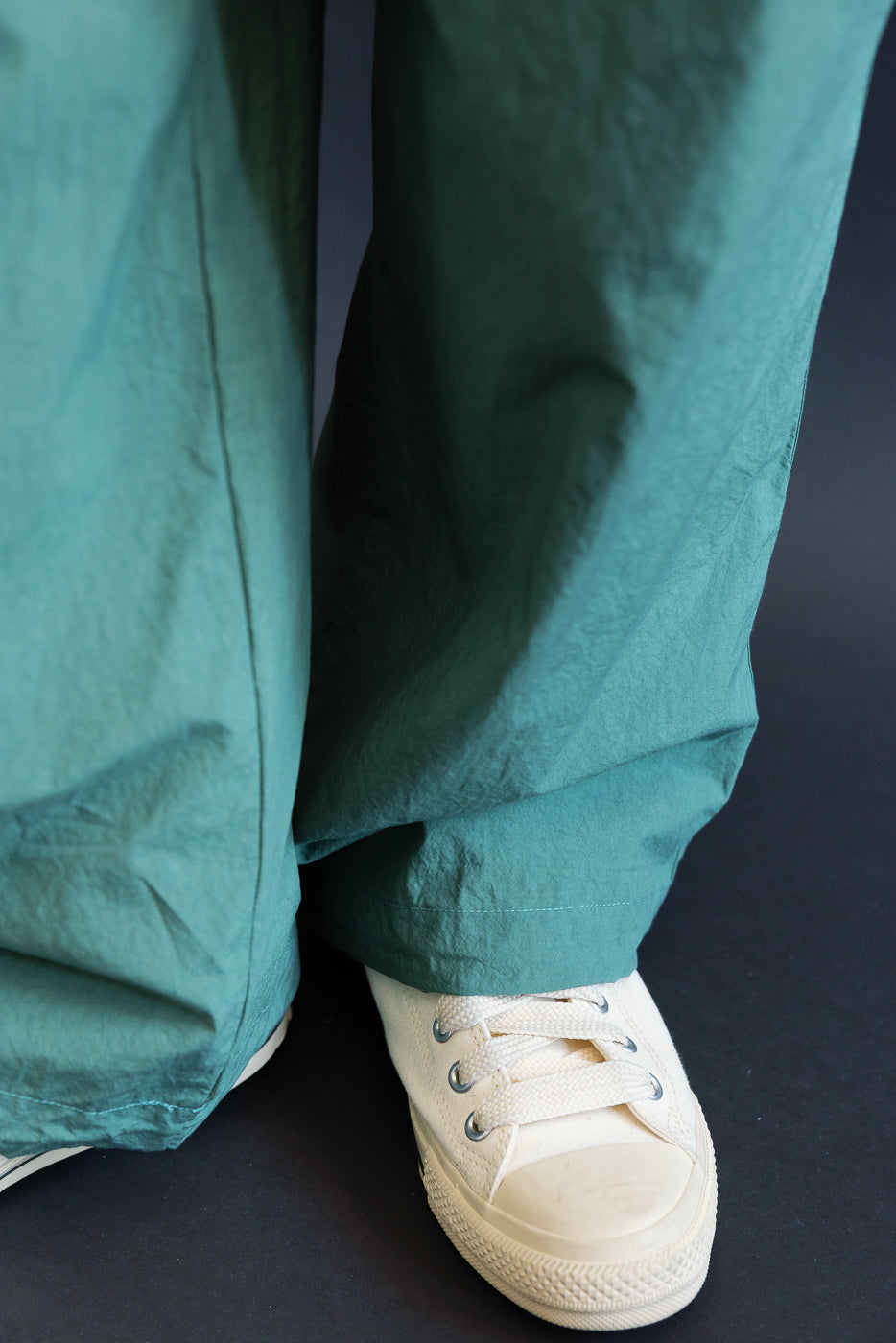 Close-up front view of teal wide-leg pants hem with cream sneakers, worn by male model