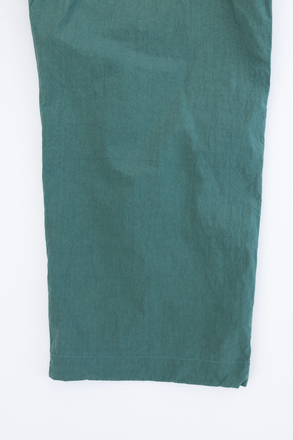 Close-up of teal garment's hem, showcasing fabric texture and stitching detail.