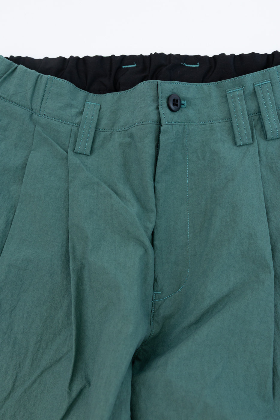 Close-up front view of teal casual pants with black button, contrast stitching, and elastic waistband detail