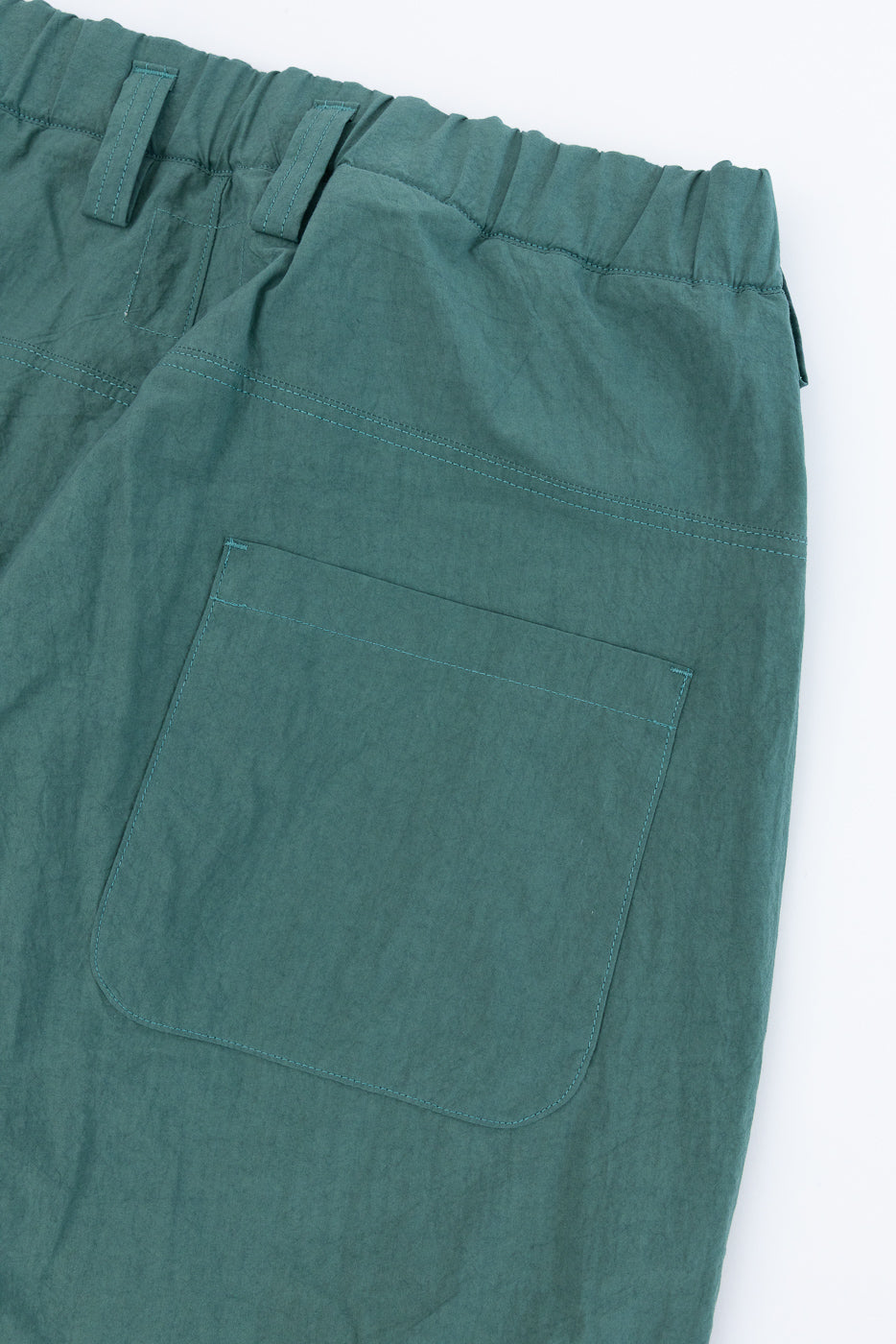 Close-up of teal pants front, elastic waist, and pocket with contrast stitching
