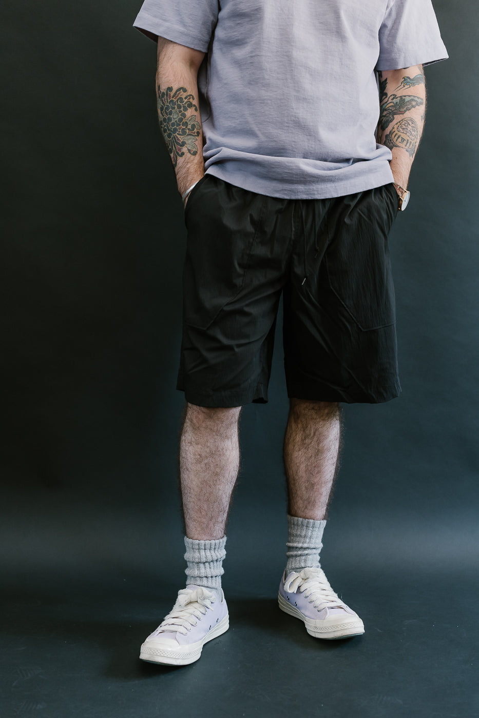 Person wearing a gray t-shirt, black shorts, white socks, and white sneakers on a dark background