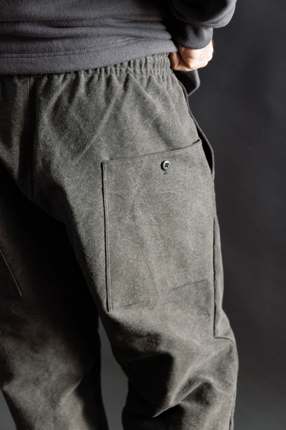 Close-up of back right side of black Jackman Sumi Ump Pants on male model, showing large button pocket and elastic waistband, model is 5'9