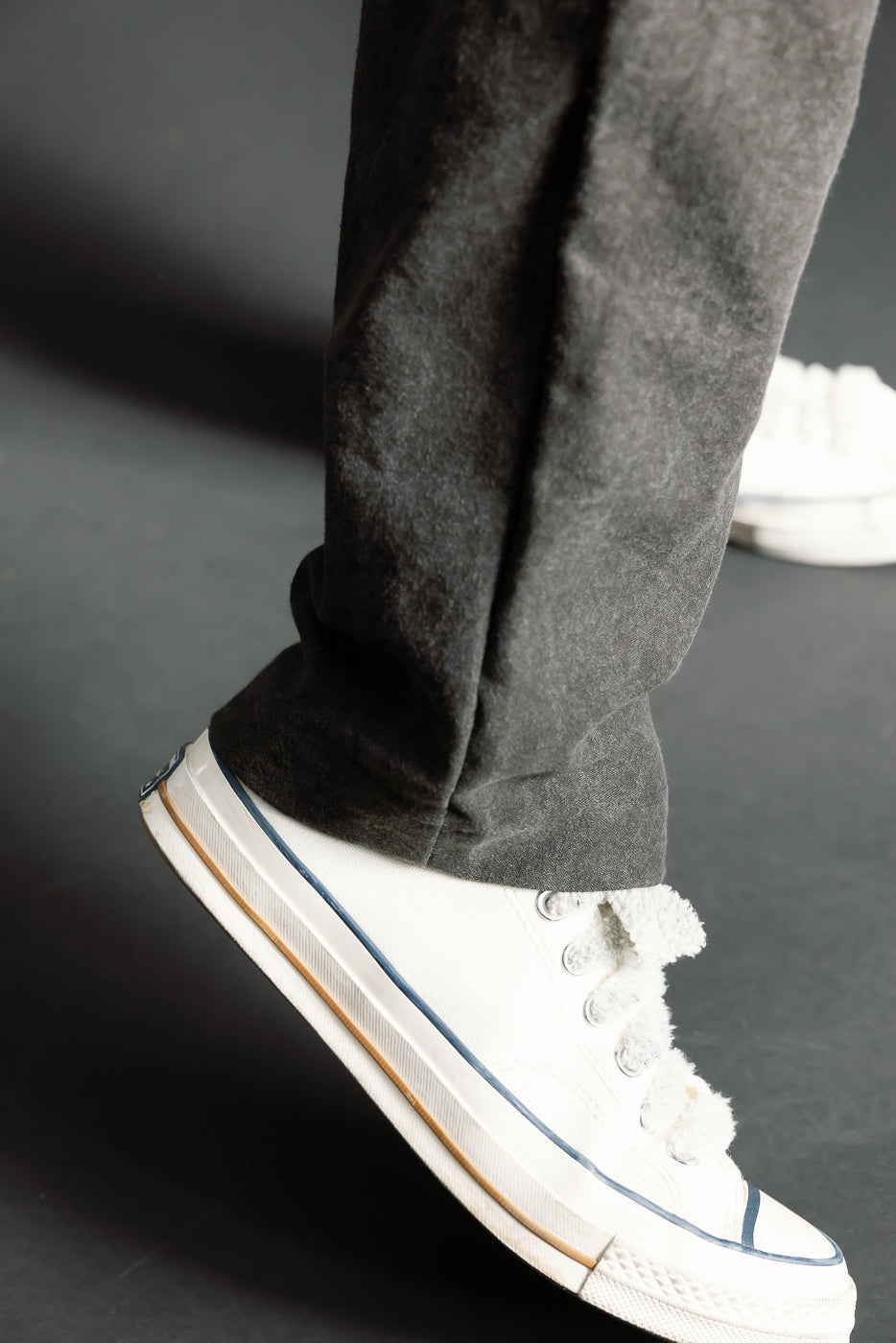 Close-up of black Sumi Ump pants hem, left side, on male model, paired with white sneaker
