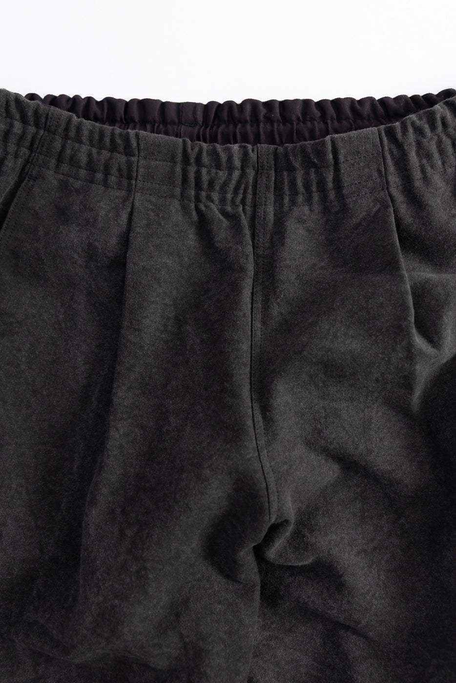 Close-up of black pants front waistband showing elastic band and textured cotton fabric, Dant