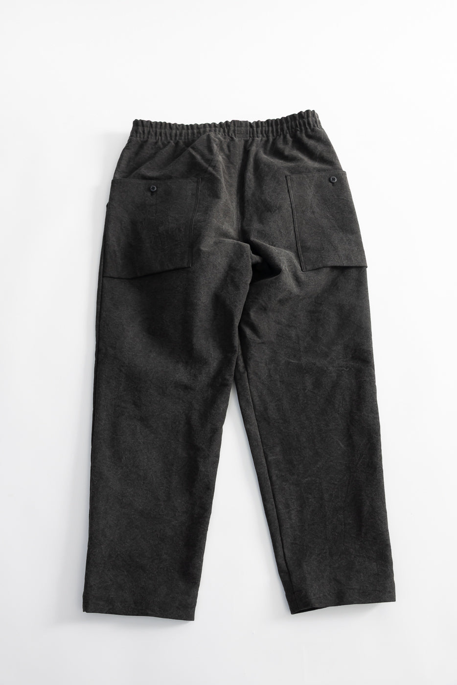 Flat lay of black pants, back view, showing elastic waistband and two buttoned rear pockets.