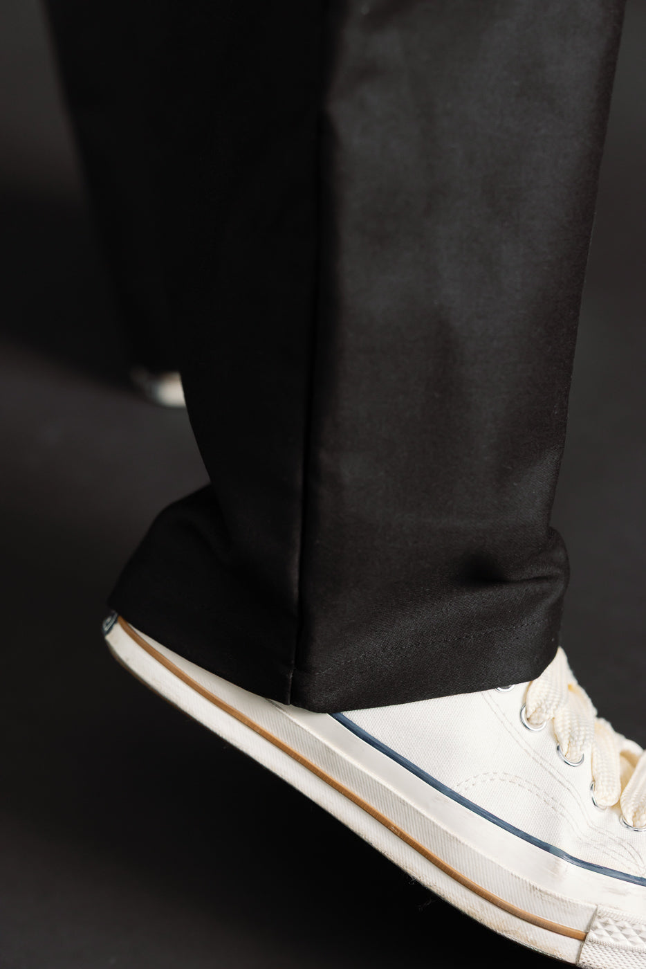 Close-up of front lower leg and hem detail on black moleskin trousers, male model, side view.