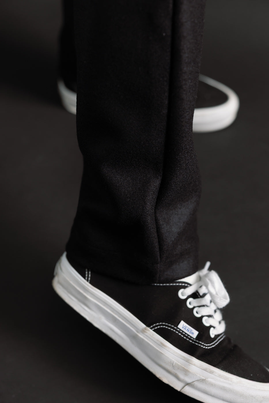 Close-up of male model's lower leg in black wool moleskin trousers, hem and side seam detail, athletic build, 5'9