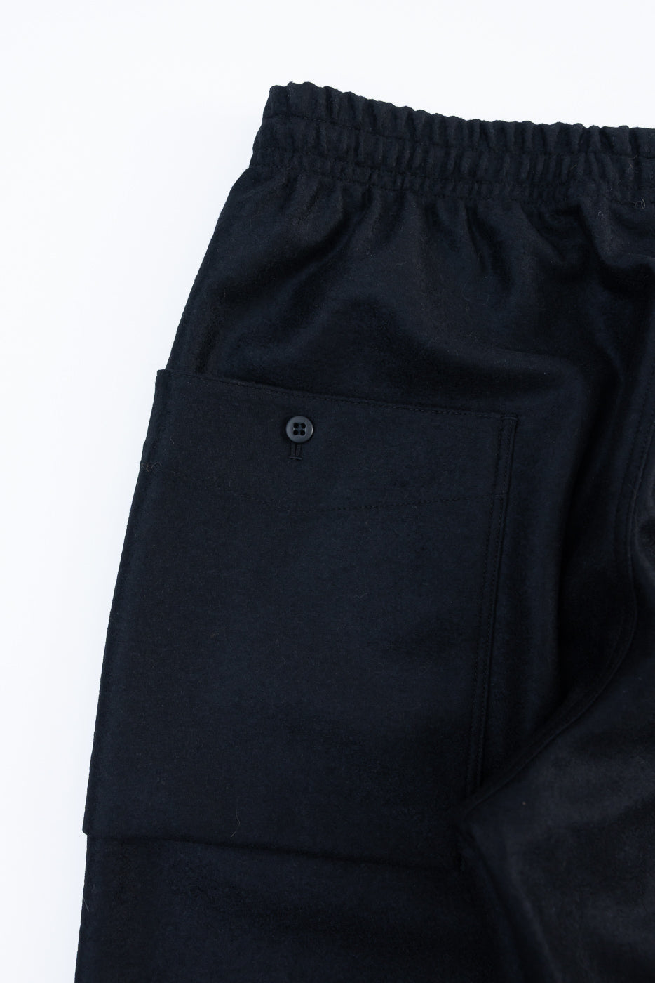 Close-up of back side of black wool moleskin trouser, showing buttoned back pocket and elastic waistband.