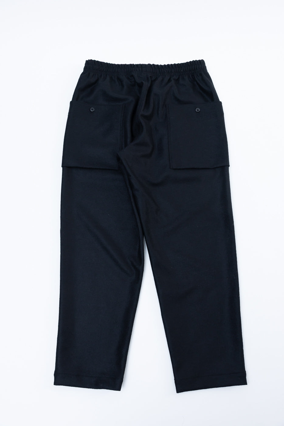 Flat lay of black wool moleskin trouser, back view, showing large buttoned rear pockets and elastic waistband.