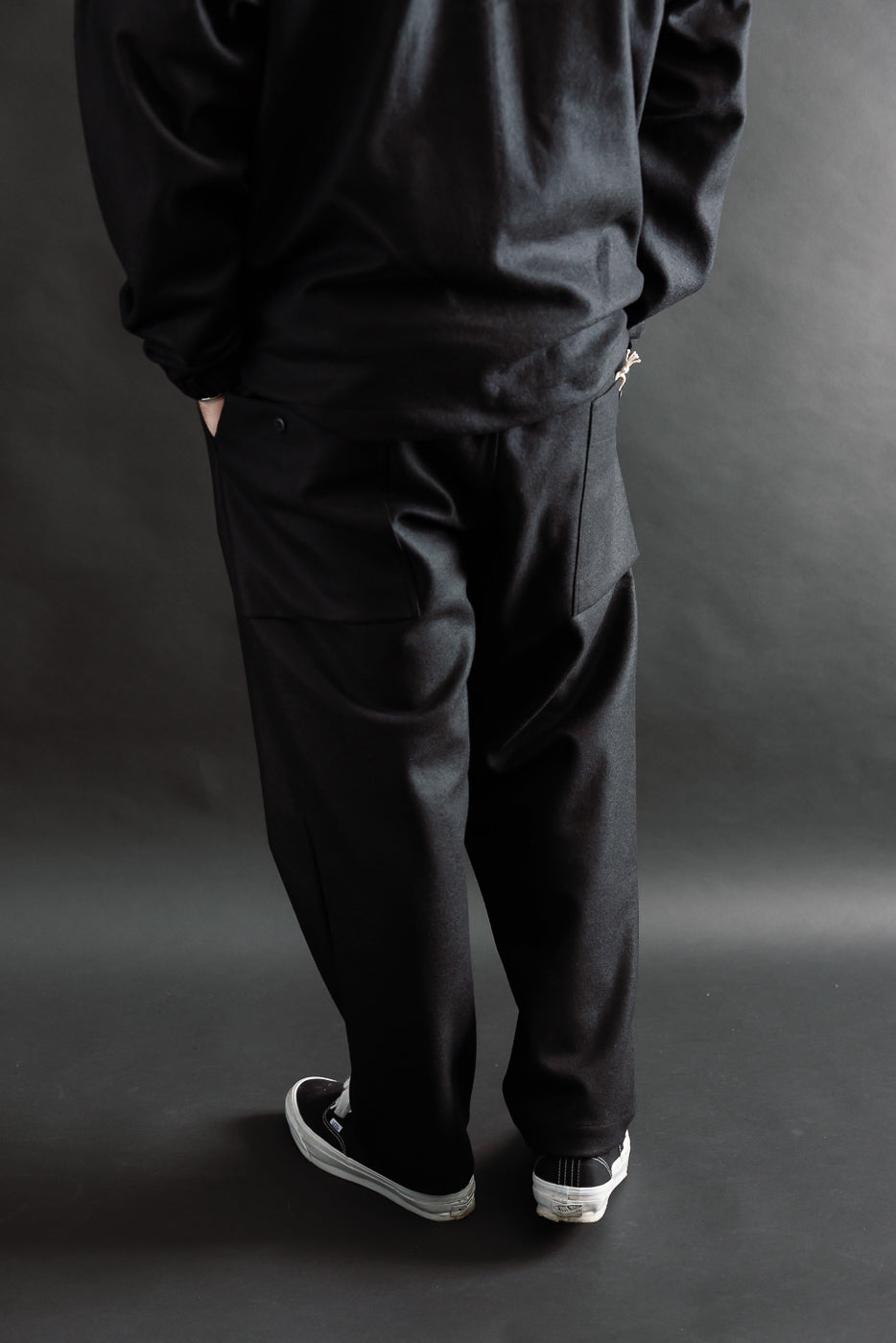 Back view, male model 5'9 165lbs athletic build wearing black wool moleskin trousers, full body.