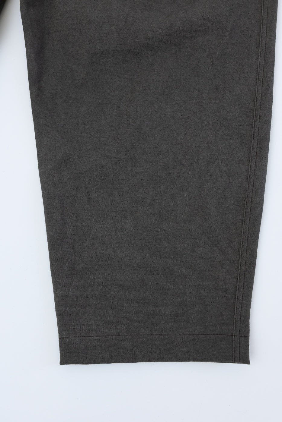Close-up of dark moss gray canvas trouser front right leg hem, fabric texture visible