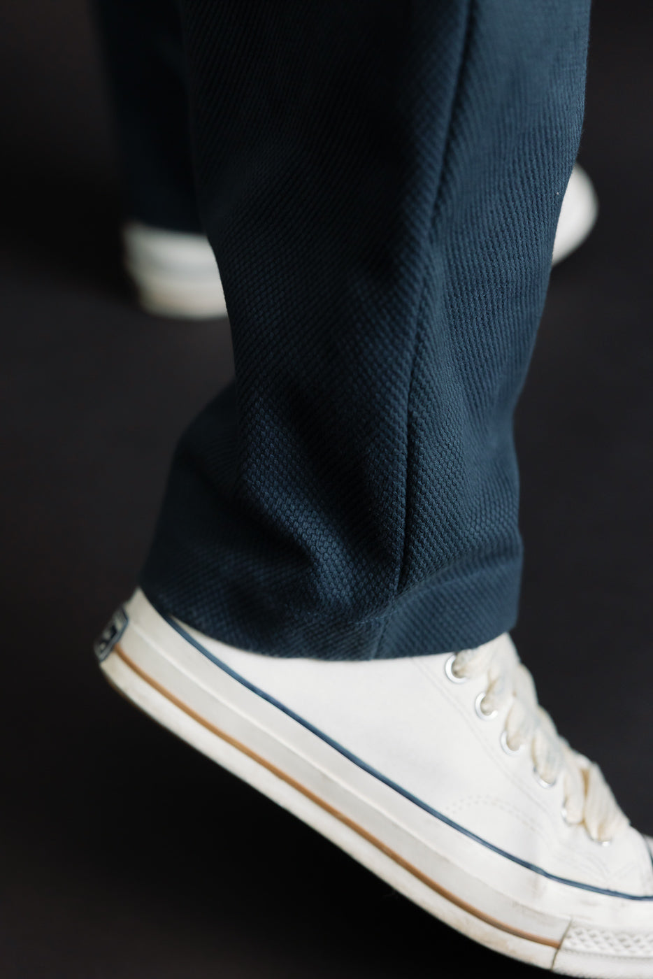 Close-up of JM4623 - Sashiko Ump Pants in 280 Iron Navy, showcasing the textured sashiko fabric resembling raw denim, worn over a white canvas sneaker with a gum-rubber sole and blue stripe.