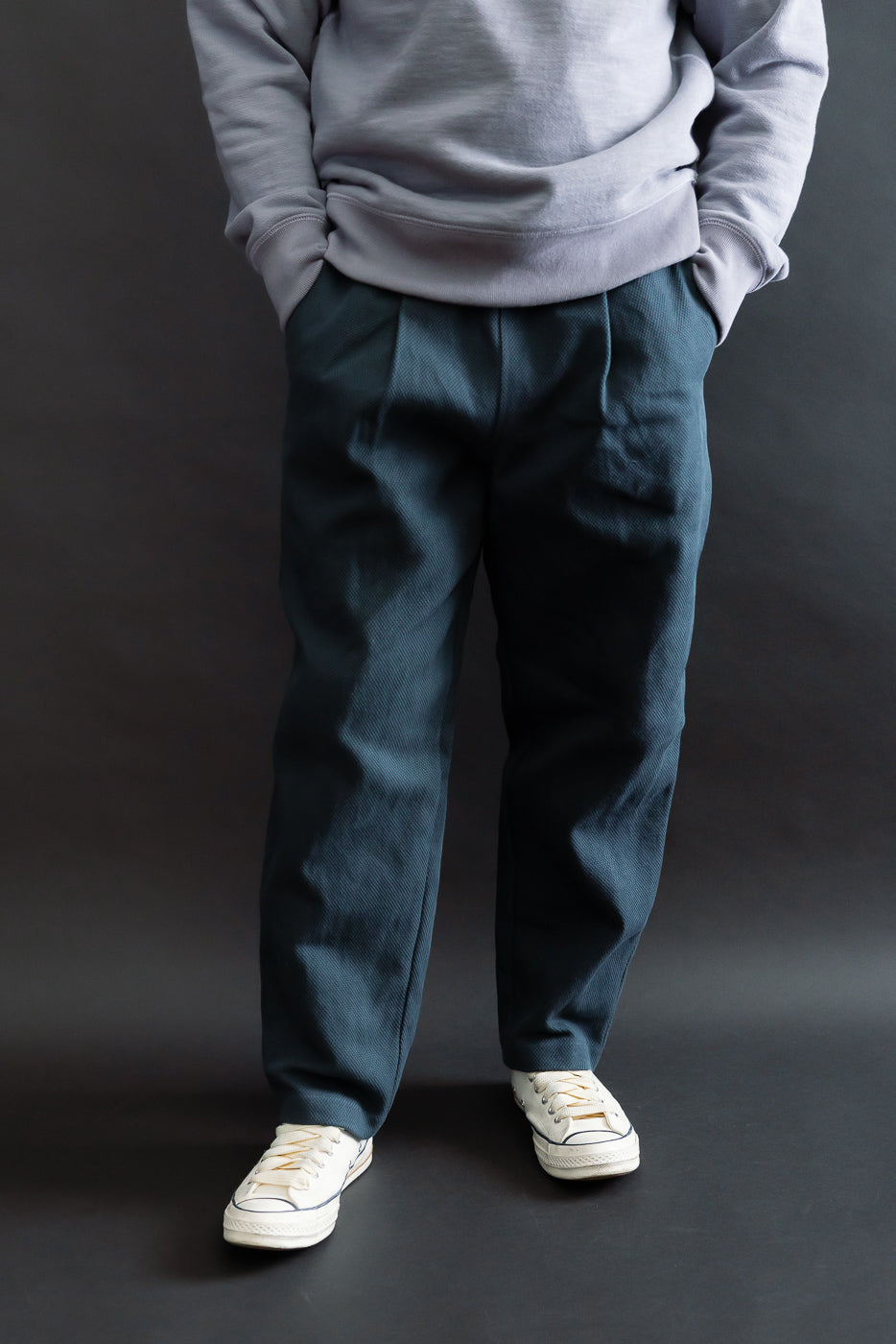 JM4623 - Sashiko Ump Pants - 280 Iron Navy feature a pleated front and large pocket, showcasing premium sashiko fabric with a structured drape, worn with a light gray sweatshirt and white sneakers.