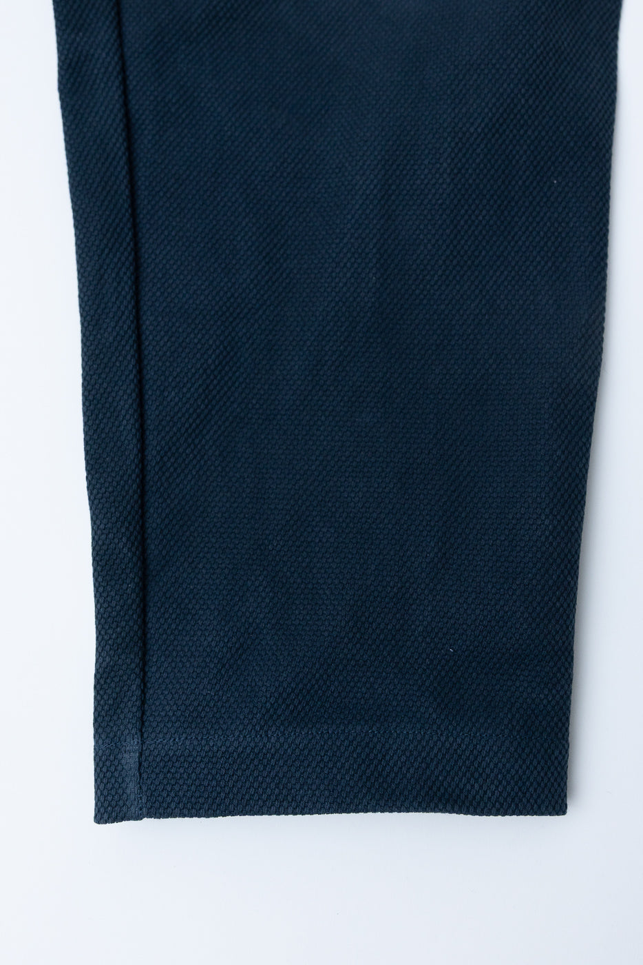 JM4623 - Sashiko Ump Pants - 280 Iron Navy close-up shows textured sashiko fabric with a straight seam and finished hem, highlighting the garment's structured drape and premium craftsmanship.