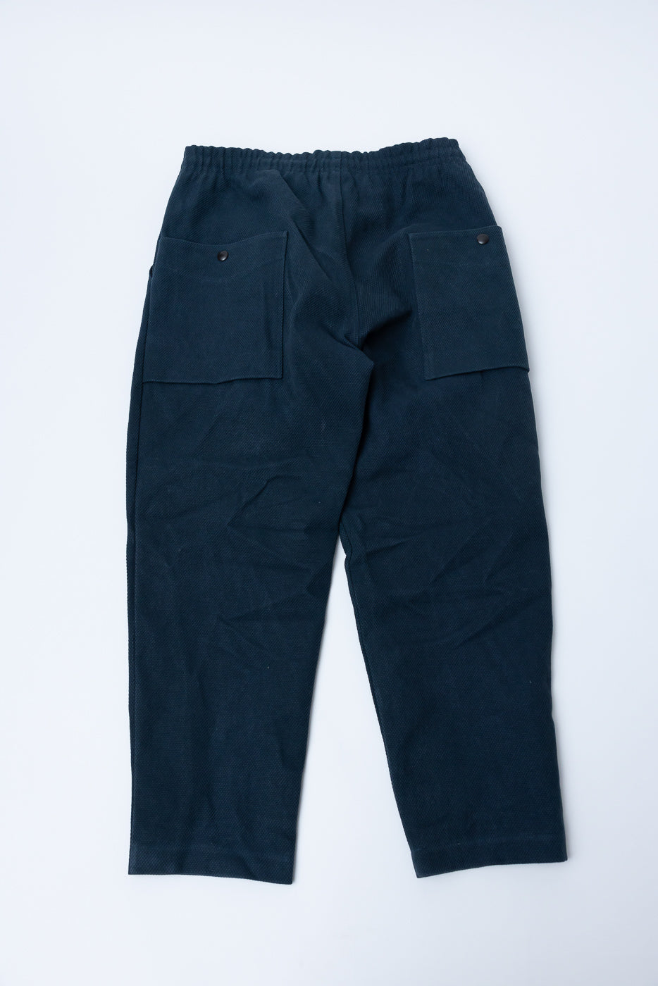 JM4623 - Sashiko Ump Pants - 280 Iron Navy, featuring a dark navy-blue sashiko fabric with elastic waistband, tapered legs, and large square patch pockets with snaps for a relaxed, utilitarian fit.