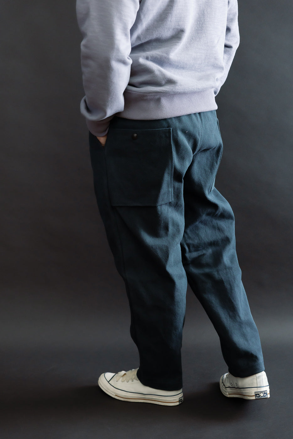 JM4623 - Sashiko Ump Pants - 280 Iron Navy, showcasing a loose fit with a back pocket flap and pleated front, styled with worn white sneakers, tucked sweatshirt, and hands in pockets.