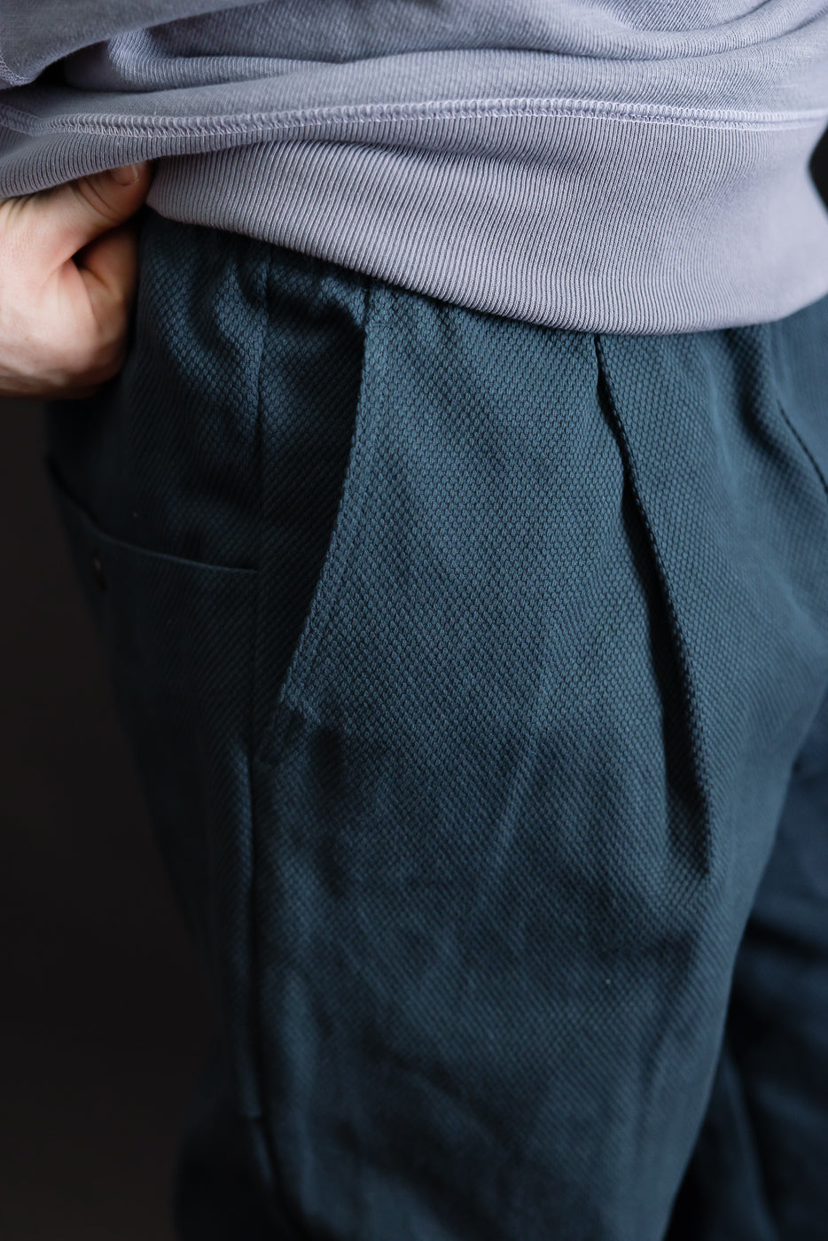 Close-up of the JM4623 - Sashiko Ump Pants in 280 Iron Navy, showcasing the textured sashiko fabric with a hand in the waistband. The pleated front and large pocket emphasize the pants' structured silhouette.