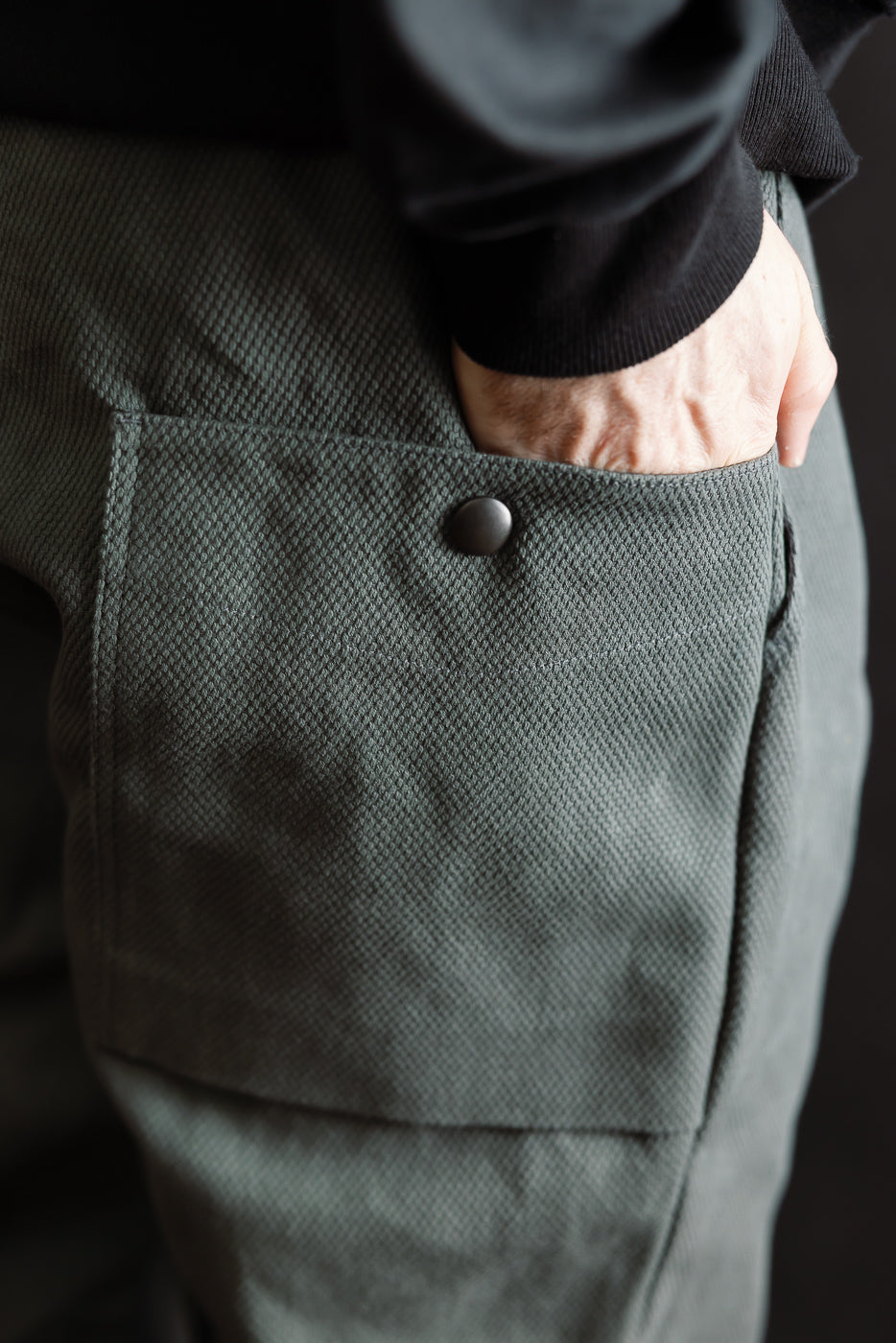 JM4623 - Sashiko Ump Pants - 333 Falcon Gray, featuring a large flap pocket with matte snap button, showcasing textured sashiko fabric with a structured, denim-like appearance, worn with a black sleeve or jacket.