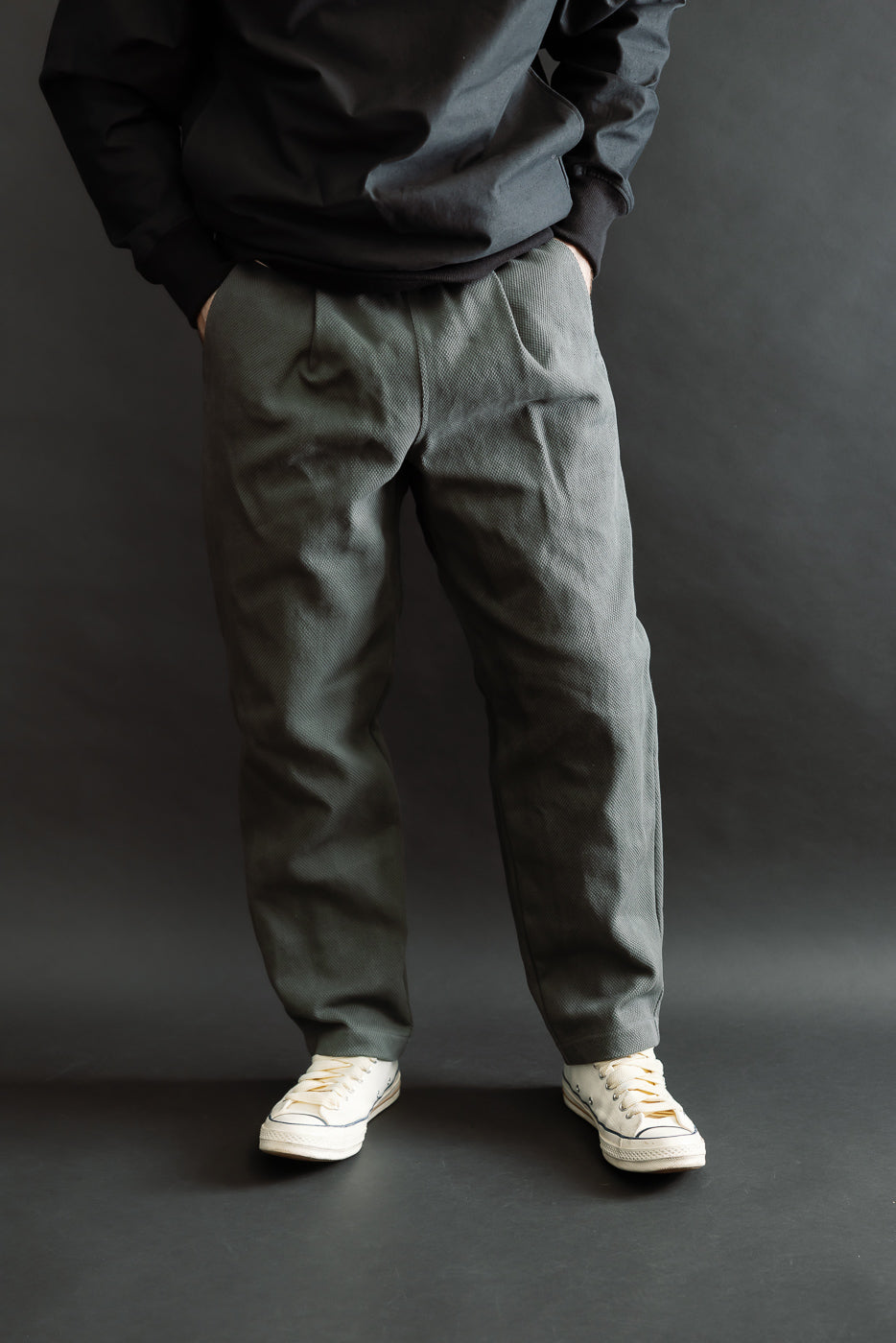JM4623 - Sashiko Ump Pants in 333 Falcon Gray, featuring a loose fit and pleated front, styled with classic low-top white canvas sneakers and a black sweatshirt hem.
