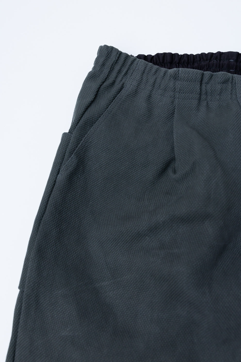 JM4623 - Sashiko Ump Pants - 333 Falcon Gray: Close-up of charcoal garment with elastic waistband and side pocket seam, showcasing a textured sashiko fabric with a structured drape and utilitarian design.