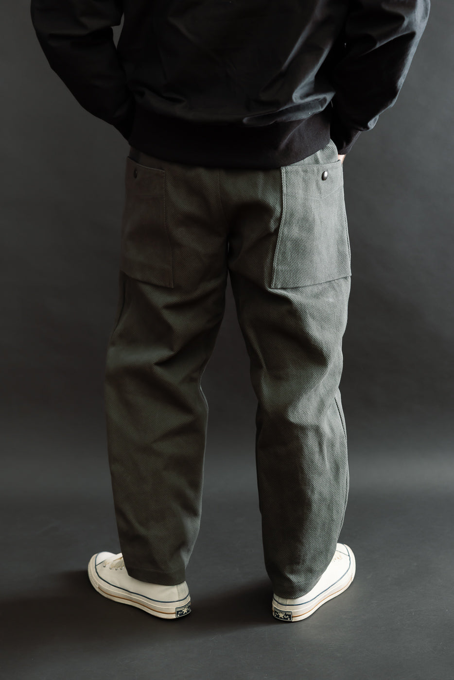 The JM4623 - Sashiko Ump Pants - 333 Falcon Gray are highlighted, showcasing their workwear-inspired design with large flap pockets and a structured drape, paired with classic white canvas sneakers.