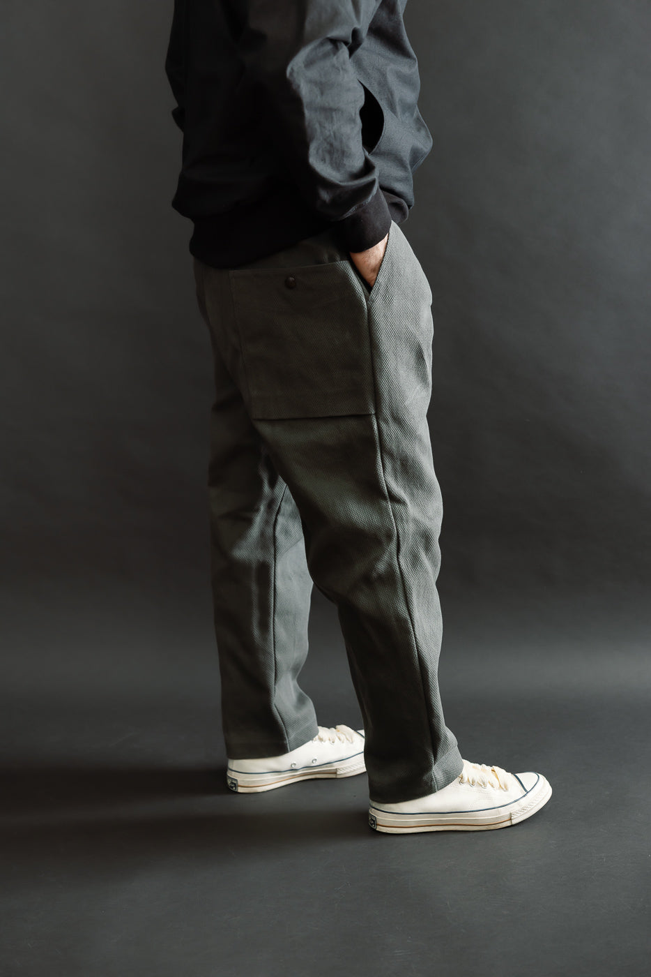 JM4623 - Sashiko Ump Pants - 333 Falcon Gray: Textured trousers with a structured drape and large pocket detail, styled with a black sweatshirt and white canvas sneakers against a dark gray backdrop.