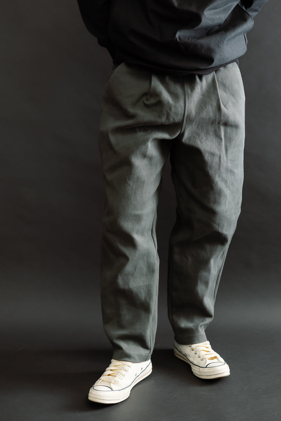 JM4623 - Sashiko Ump Pants - 333 Falcon Gray are loose-cut, textured trousers with a pleated front and large waist-to-hip pocket, paired with off-white canvas sneakers.
