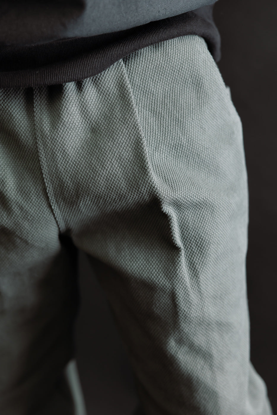 JM4623 - Sashiko Ump Pants - 333 Falcon Gray feature a close-up of the waistband and hip area, showcasing the ribbed knit top's texture over light-gray/green textured sashiko fabric trousers.
