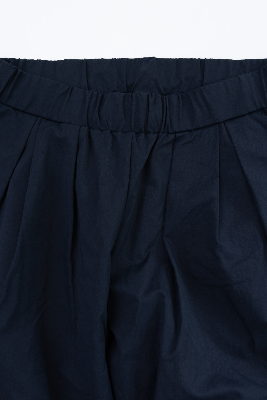 Close-up front view of navy pleated shorts with elastic waistband, showcasing fabric texture and stitching details.