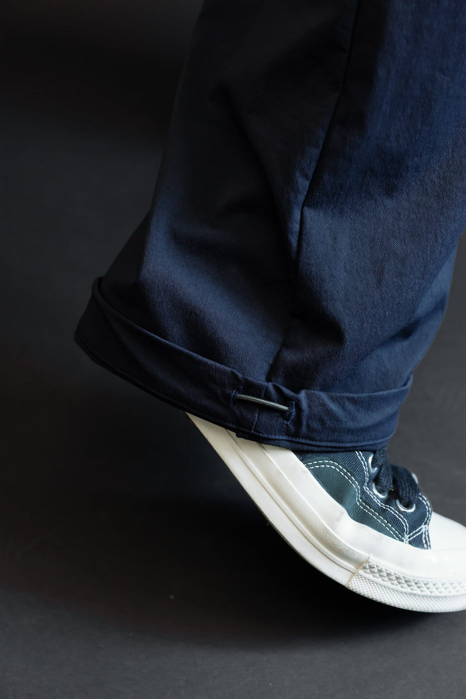 Close-up of navy pants hem with cuffed detail, worn by male model, paired with dark sneakers