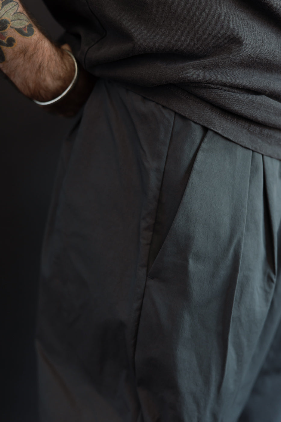 Close-up of male model's side, showing dark pleated pants with fabric texture, 5'9