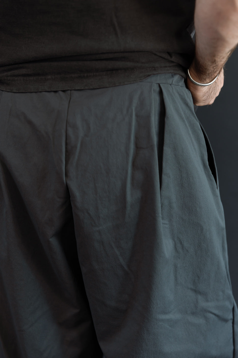 Close-up front view of dark gray pleated pants on male model, 5'9
