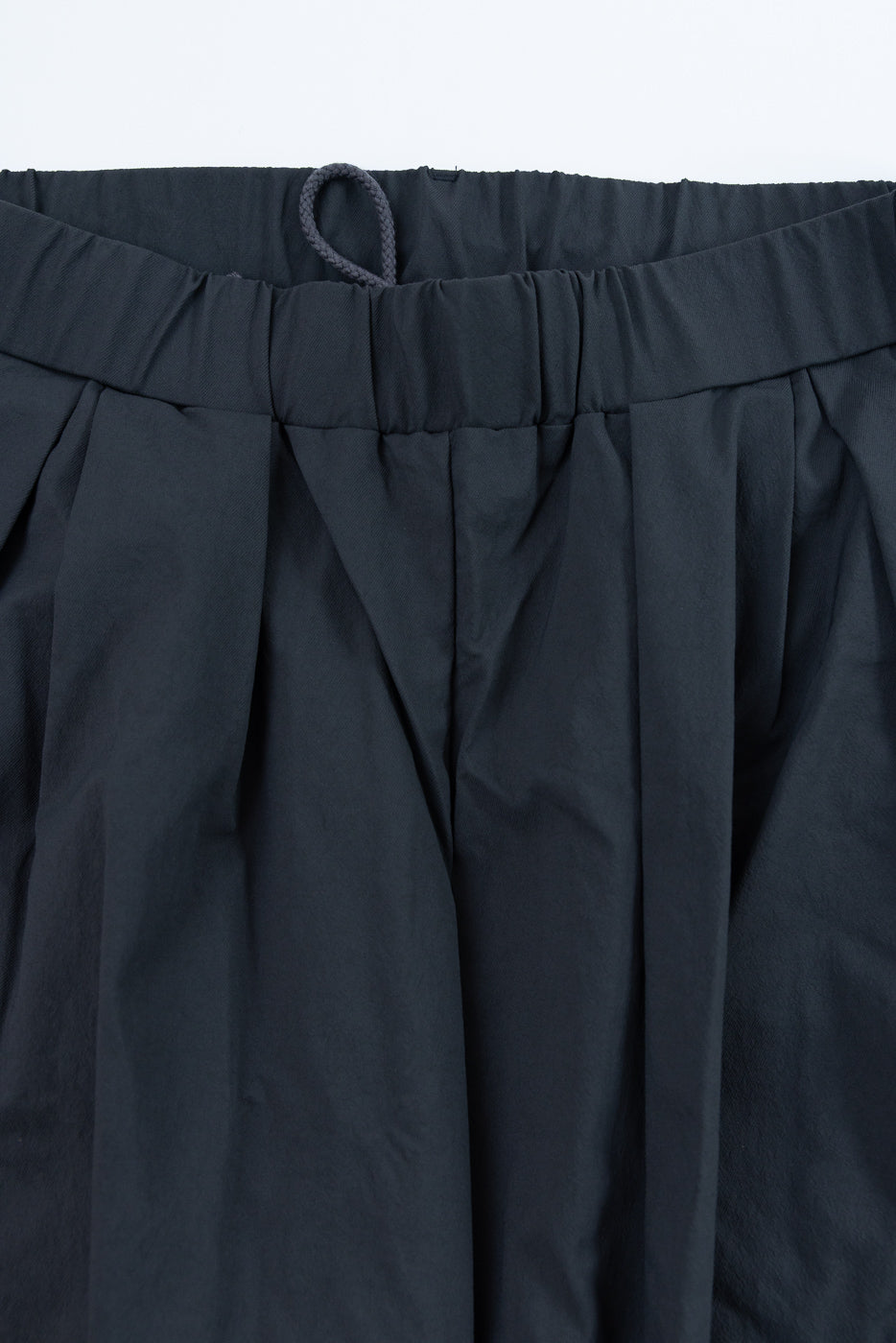 Close-up front view of dark navy pleated shorts waistband with drawstring, showcasing fabric texture and elastic detail.