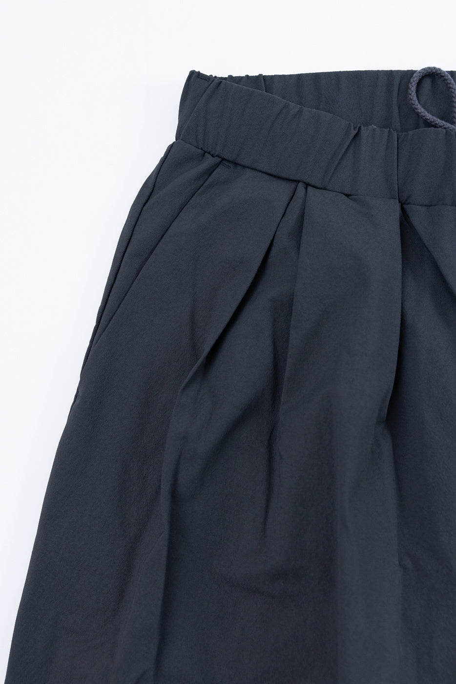 Close-up front view of dark gray pleated pants with elastic waistband and drawstring, showcasing fabric texture and tailored fit.