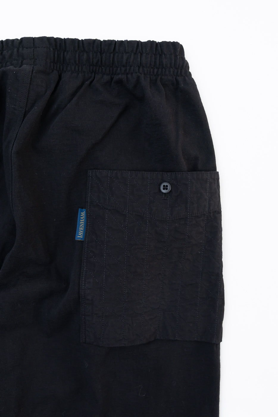 Close-up front view of black cargo shorts showing a side pocket with button detail and blue tag.