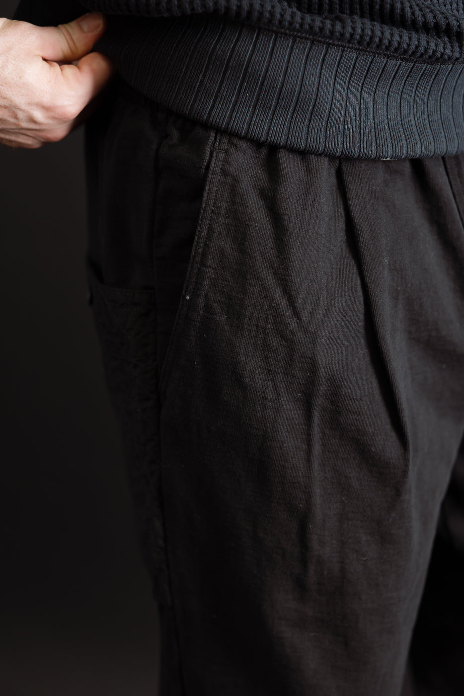 Close-up side view of dark brown textured fabric trousers on a male model, showing pocket detail.