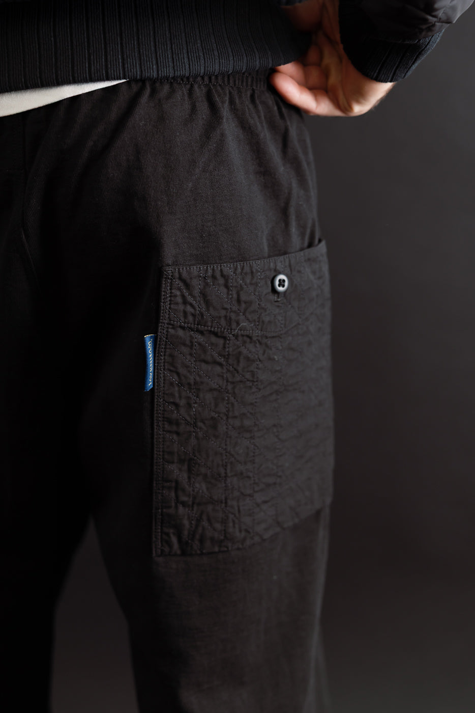 Close-up of the back left pocket and fabric texture on black casual trousers worn by a male model.