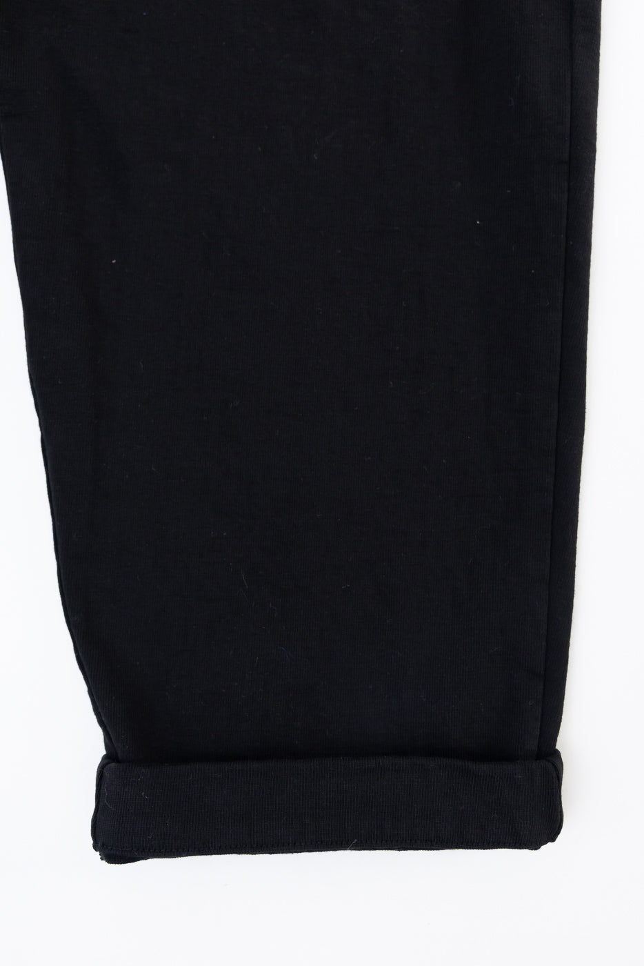 Close-up of the rolled cuff and hem of black fabric trousers on a white background.