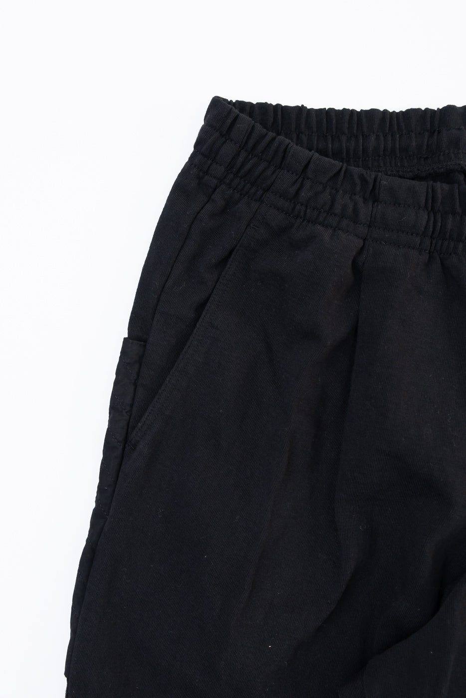 Close-up front view of black cotton shorts showing elastic waistband and side pocket detail.