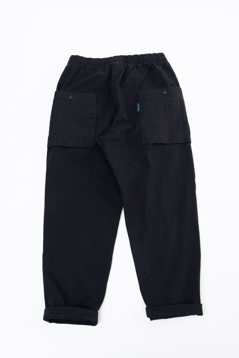 Flat lay, back view of black cargo trousers featuring large utility pockets and elastic waistband.