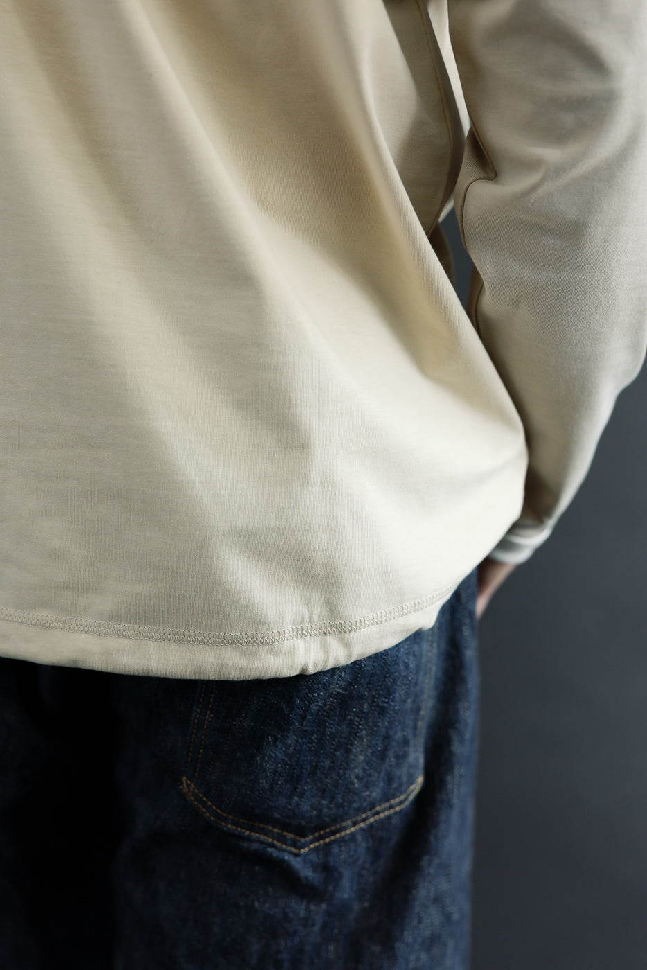 Close-up of male model's side, showing cream long-sleeve shirt hem and selvedge denim pocket detail