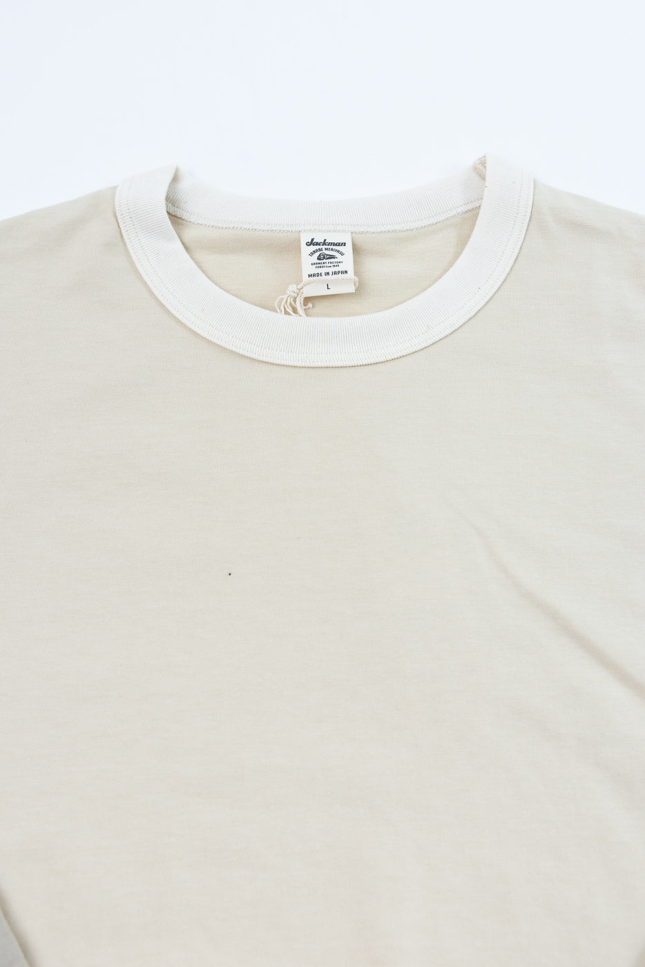 Close-up front view of cream long sleeve tee, showing ribbed collar and 'Made in Japan' tag detail.