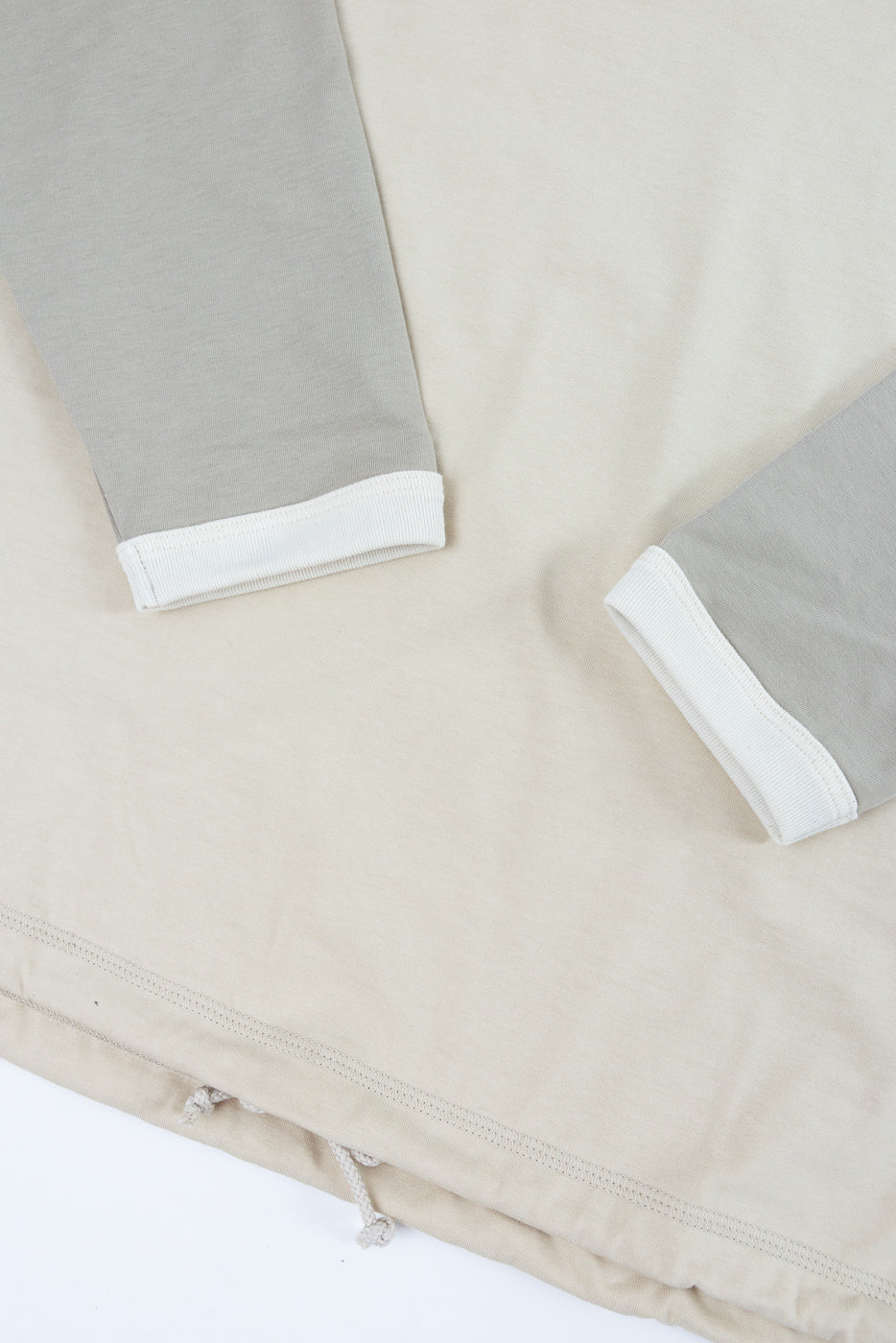 Close-up of beige long-sleeve shirt with gray sleeves, white ribbed cuffs, and drawstring hem