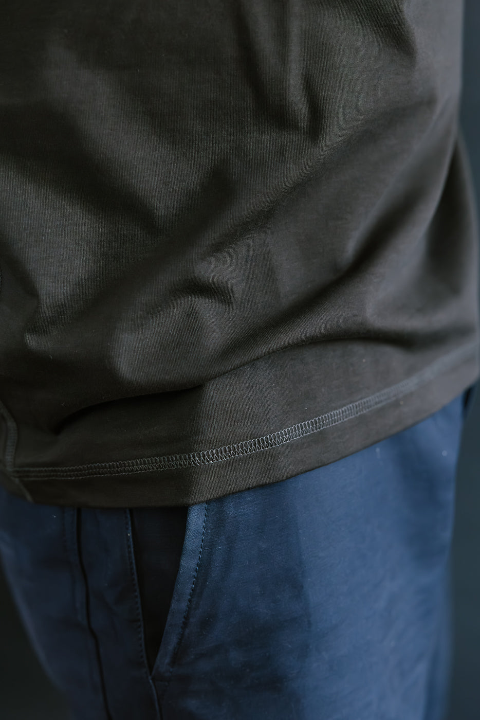 Close-up of a person wearing a dark green shirt and blue pants against a neutral background