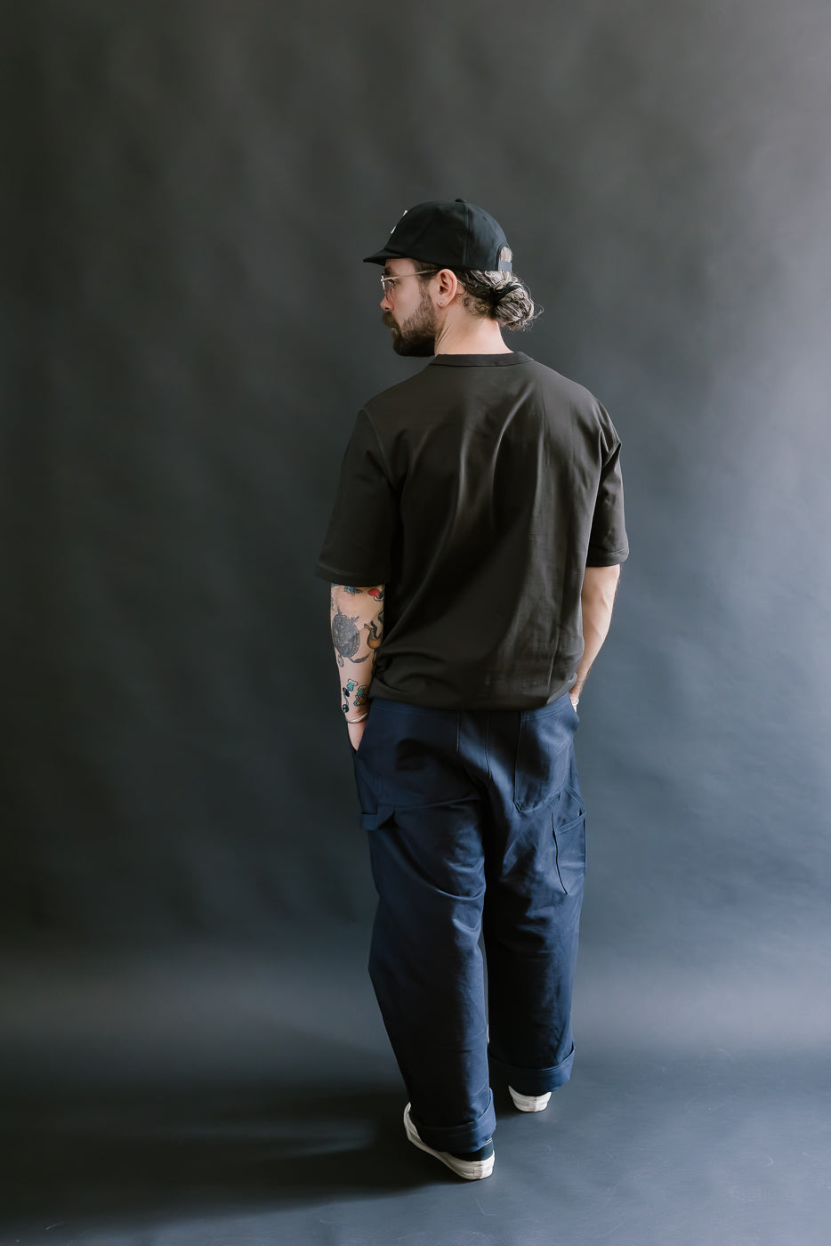 Man wearing a black t-shirt and blue cargo pants against a dark gray background