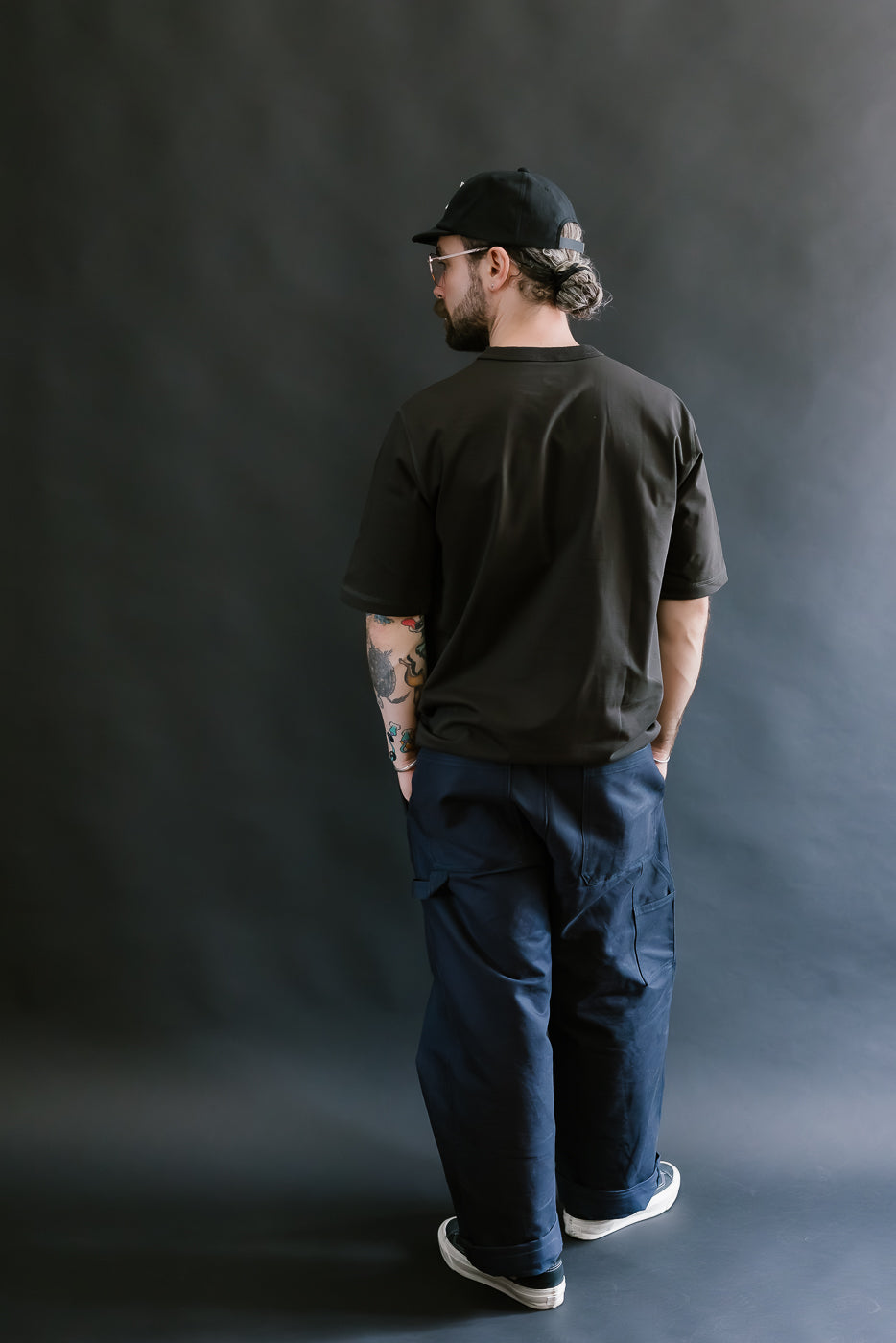 Man wearing a black t-shirt and blue pants against a dark gray background