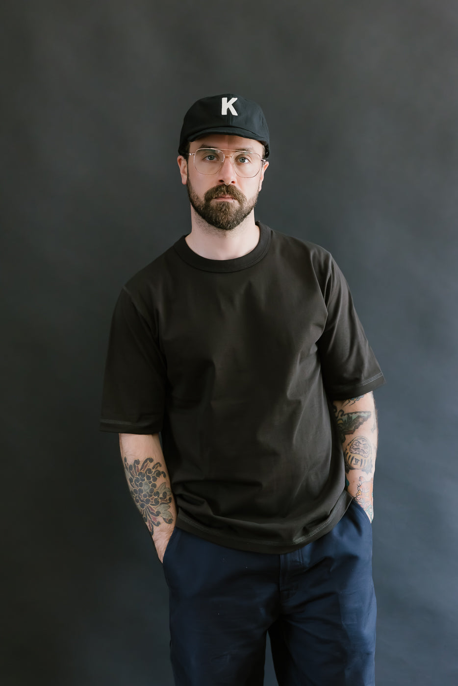 Man wearing a black t-shirt and cap with a 'K' logo against a dark background