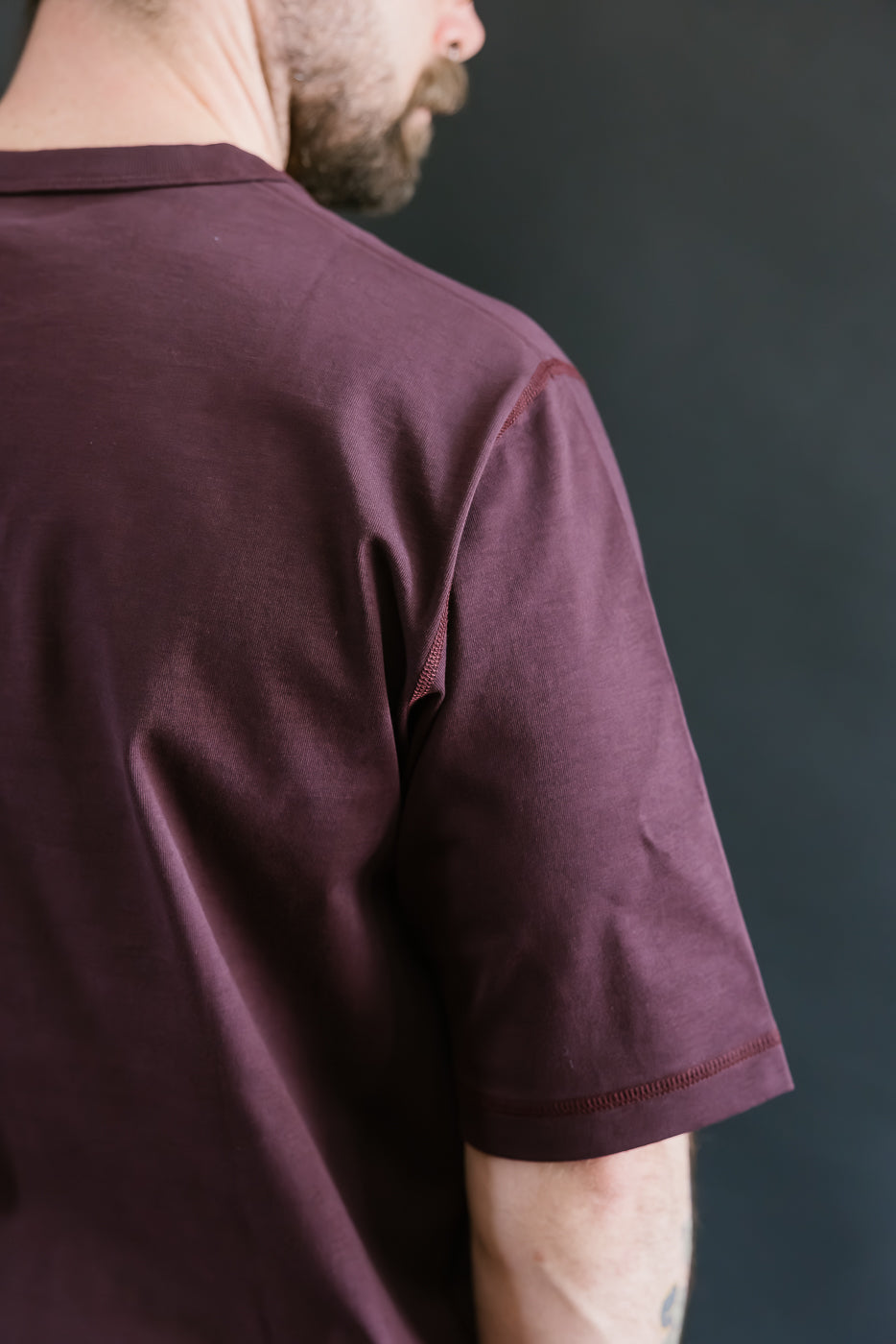 Person wearing a maroon t-shirt against a dark background