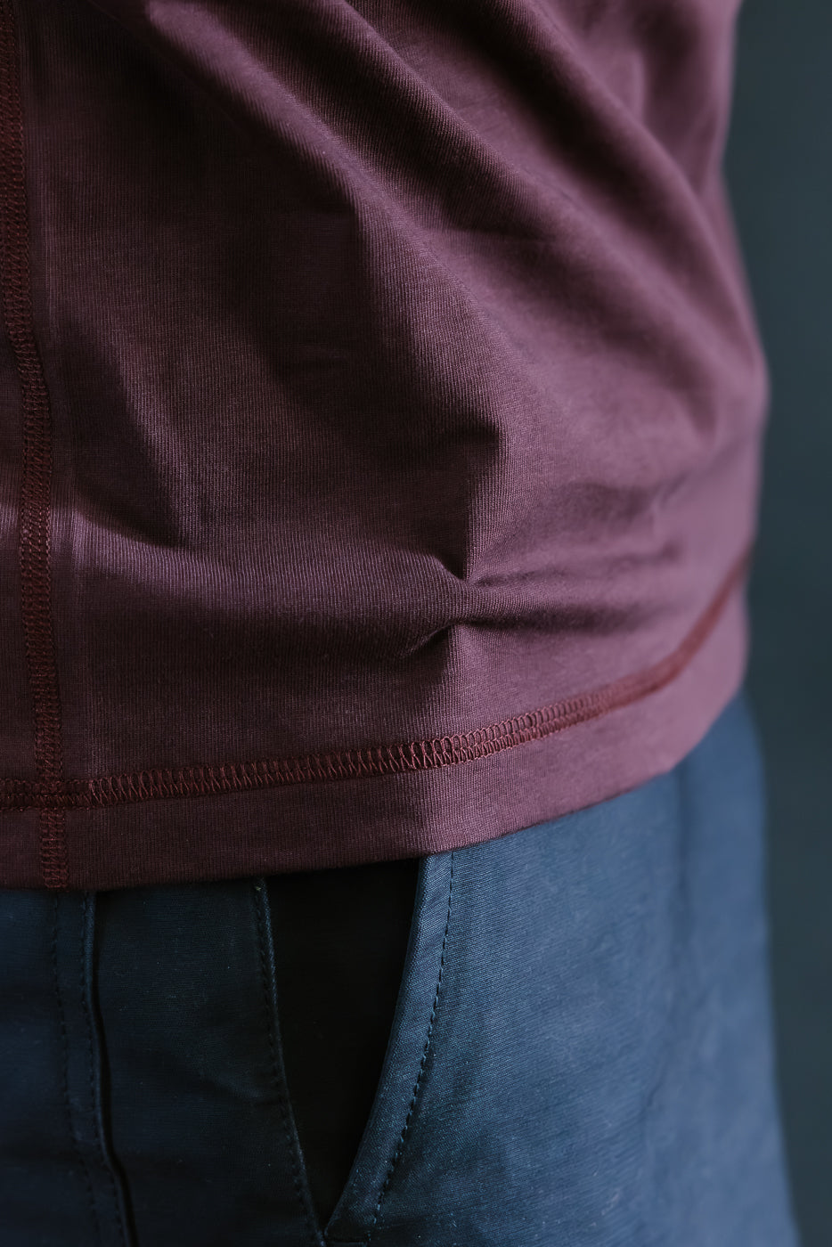 Close-up of a person wearing a maroon long-sleeve shirt and blue pants against a dark background